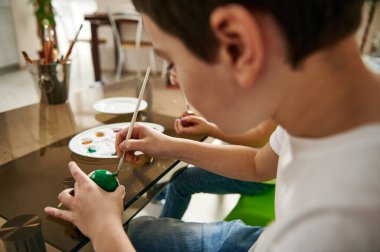 Paskalya Yumurtası 'nı evde yeşil gouache ile boyayan ve Paskalya kutlamalarına hazırlanan bir öğrencinin yakın çekimi.