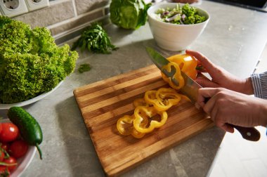 Bıçak tutan ve yüzüklere sarı biber kesen kadın eller. Yüksek açı. Yakın çekim..