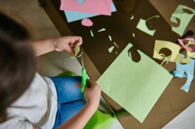 Renkli kâğıttan şekiller kesen tanınmayan küçük bir kızın yakın çekimi. Çocukların yaratıcı hobisi