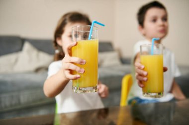 İki tatlı çocuk ellerinde portakal suyu bardağıyla onları kameraya gösteriyor.