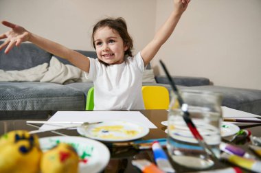 Saçları örgülü şirin küçük bir kız masada oturuyor ve çizim ya da resim yapmaktan zevk alıyor. Çocukların yaratıcılık kavramı. Sanat eğitimi
