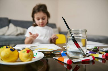 Saçları örgülü şirin küçük bir kız masada oturuyor, resim yapıyor ya da resim yapıyor. Çocukların yaratıcılık kavramı. Sanat eğitimi