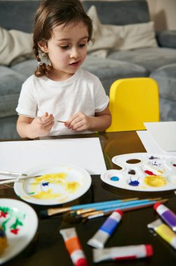 Masada oturan sevimli küçük kız çizim yapmak ya da resim yapmak için ellerini boş bir kağıda koyuyor. Çocukların yaratıcılık kavramı. Sanat eğitimi