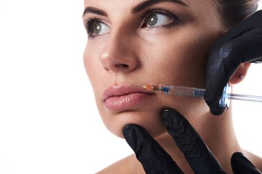 Beyaz arka planda izole edilmiş çekici bir kadının yüzü ve eldivenli güzellik uzmanlarının elleri dudaklara güzellik iğnesi yapıyor. Enjeksiyon kozmetolojisinde dudak büyütme kavramı