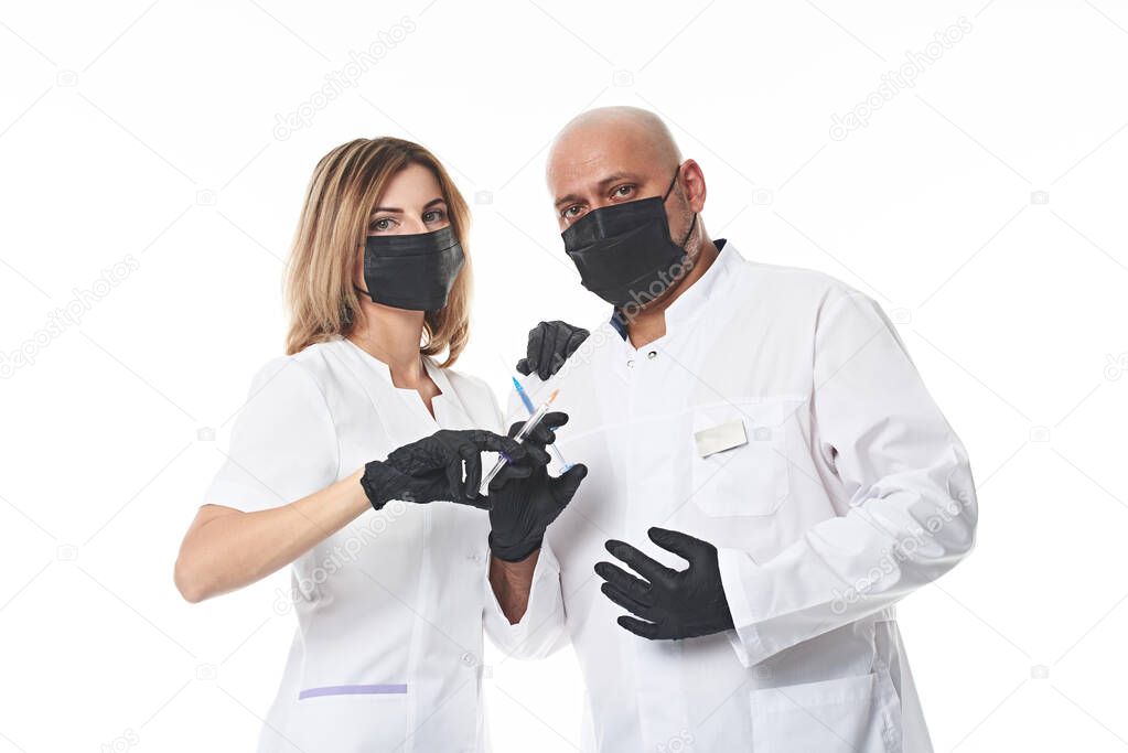 Two doctors in medical uniform are standing next to each other with syringes in their hands, wearing a medical protective mask and looking at the camera. Isolated on white background with copy space