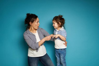 Anne ve kızı taş-kağıt-makas oynuyorlar. Annelik ve çocukluk kavramı. Mavi arkaplan ve kopyalama alanı