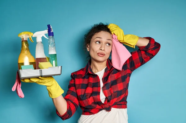 Exhausted beautiful woman housewife wiping her face with a pink cleaning rag, looking away, exhausted after house working. Housework and chores. Concept on blue background with copy space.