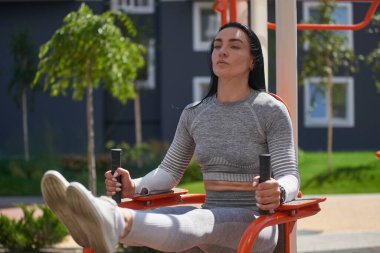 Düz göbekli genç bir kadın baskıyı sallarken dengesiz demirlerde bacaklarını kaldırıyor. Ön manzara. Açık hava eğitimi kavramı