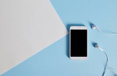 Beyaz cep telefonu ve kulaklıkların düz kompozisyonu beyaz bir kâğıt kağıdın yanında mavi arka planda yatıyordu. Boşluğu kopyala
