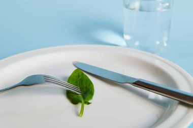 Tabakta ıspanak yaprağı, çatal, bıçak ve bardakta mavi arka planda su. Diyet ve sağlıklı beslenme konsepti. Yakın plan.