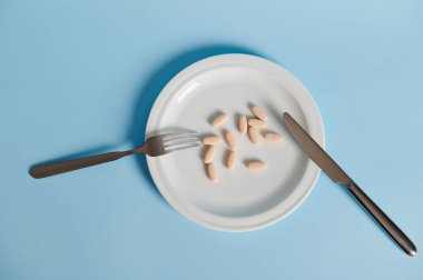 Çatal, bıçak ve haplarla bembeyaz tabakta düz bir bileşim vardı. Kopya alanı ile mavi arkaplanda izole