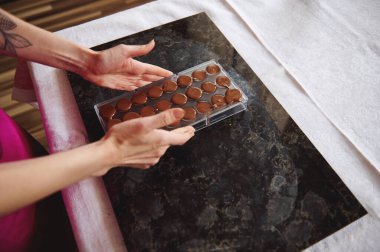 Close-up of female hands holding chocolate molds full of liquid heated chocolate mass. Preparing chocolates for celebrating World Chocolate Day clipart