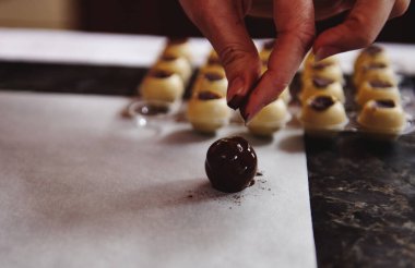 Çikolata trüf mantarı üzerinde parşömen kabartma kağıdına odaklan çikolata kalıplarının arka planına ve hazır şekerin üzerine kakao tozu serpiştiren pasta şefinin eline.
