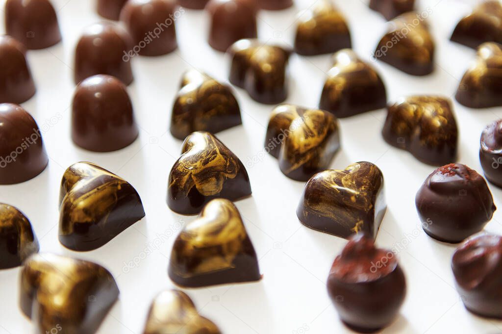 Assortment of beautiful luxury Belgian chocolate candies, truffles and pralines with golden ornament in heart shape on a white background
