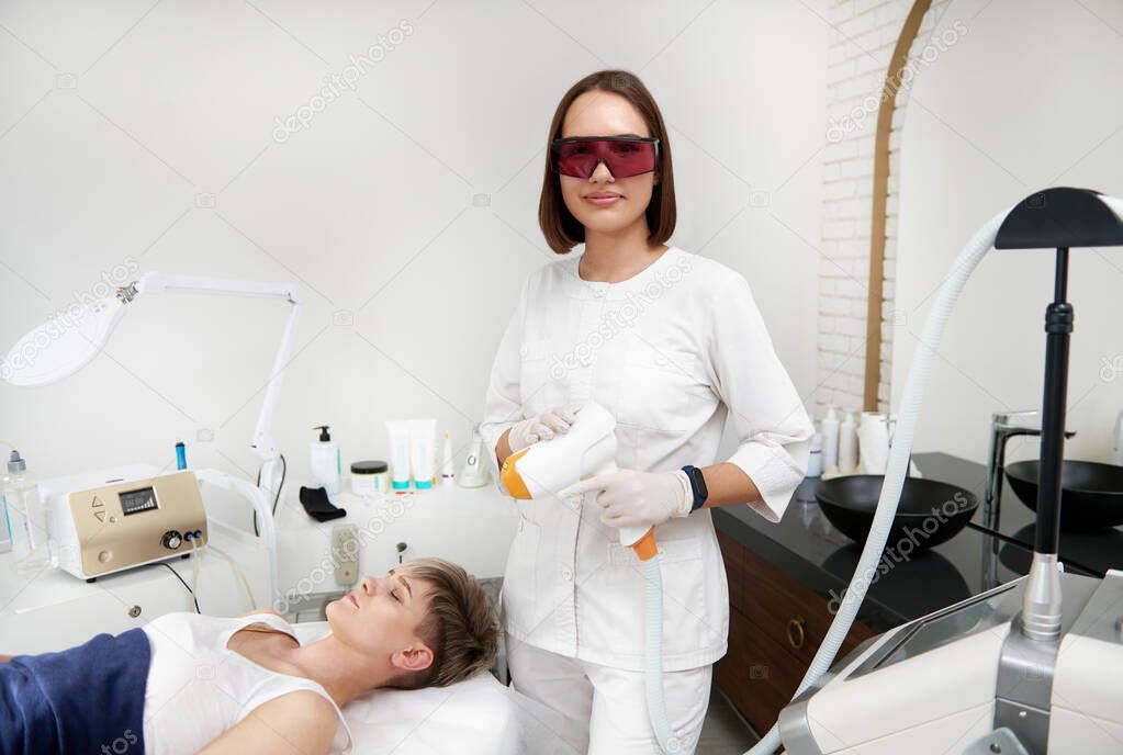 The beautician holding a laser device in hands for rejuvenation in a beauty salon. Elos epilation procedure on the face of a young woman. Facial skin care. Hardware ipl cosmetology