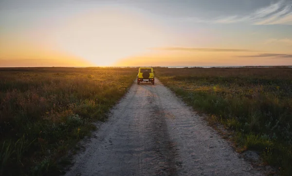 A car moving along a country steppe road in the light of a beautiful sunset sky. The concept of travel and explore the nature by car