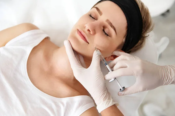 Doctor-cosmetologist making beauty injection on the face of a young woman at SPA center. Concept of injection cosmetology for rejuvenation and correction skin defects