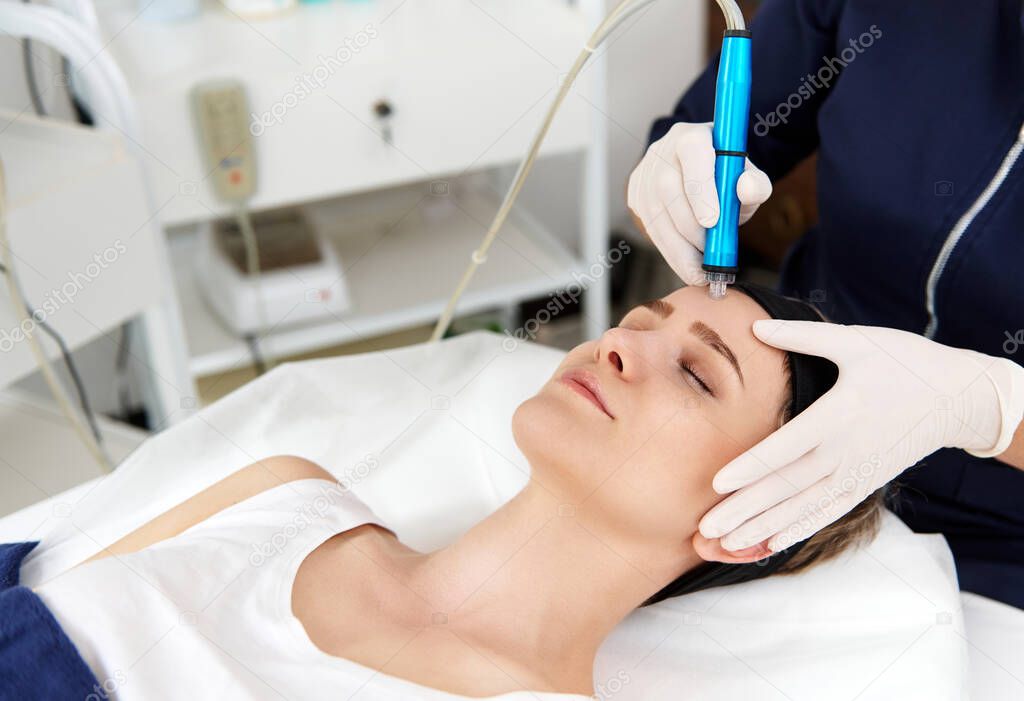 Close-up of a aesthetician using an aqua peel to clean and exfoliate a woman's face. Removal of skin slags in the pores using special equipment in hardware cosmetology.