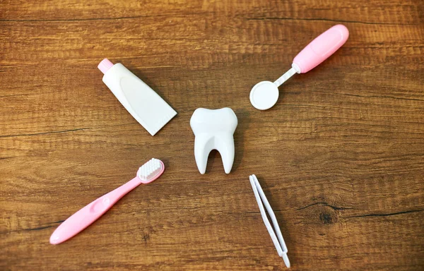 Flat Lay composition with toy dental tools for oral care. A toy white tooth, a toy dental mirror, forceps, toothpaste and toothbrush on a wooden background. Oral care concept for children