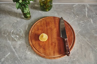 Mutfak tezgahında nane şekeri olan bir bardağın yanındaki yuvarlak ahşap mutfak tahtasına limonu ikiye bölen düz bir kompozisyonda yatıyordu.