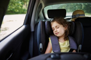Little girl sleeps in a booster seat in the car. Child safety seat.. Safe movement of children in the car clipart