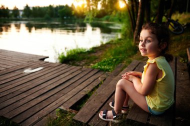 Rıhtımda dinlenen çekici bir kızın yan portresi nehir kıyısının arka planına bakıyor. Kamp, yaz temaları.