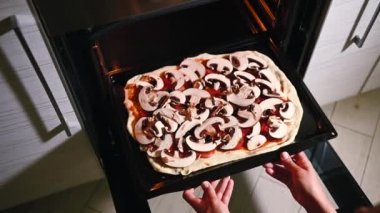 Kadın şef ev kadınının fırına pizza koyarkenki yüksek açılı görüntüsü. Video görüntüleri.