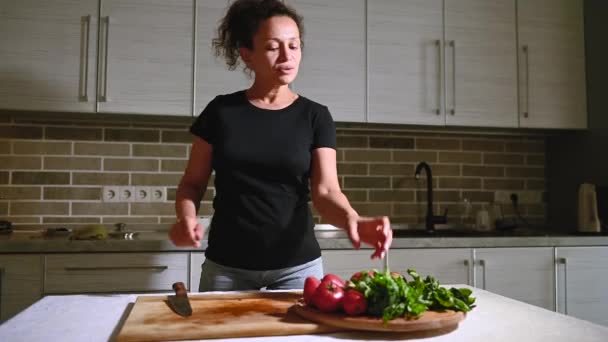 キッチンの木の板の上でトマトをカットしながら踊る幸せなアフリカ系アメリカ人女性 ビデオ映像 — ストック動画