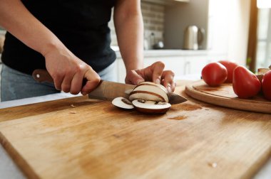 Ahşap mutfak tahtasının üstünde mantar doğrarken aşçı ya da ev hanımı ellerinin yakın çekimi.