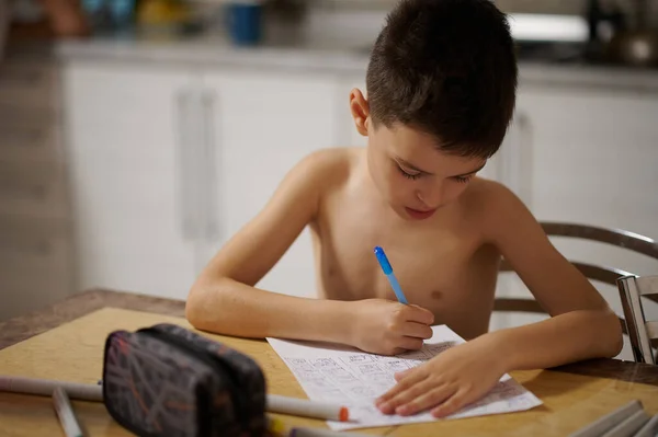 Adorable teenage boy drawing anime comics on a sheet of white paper at home