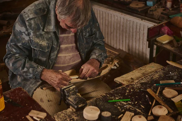 Master-class on making wooden toys. Hands of a master with a chisel and a wooden workpiece.