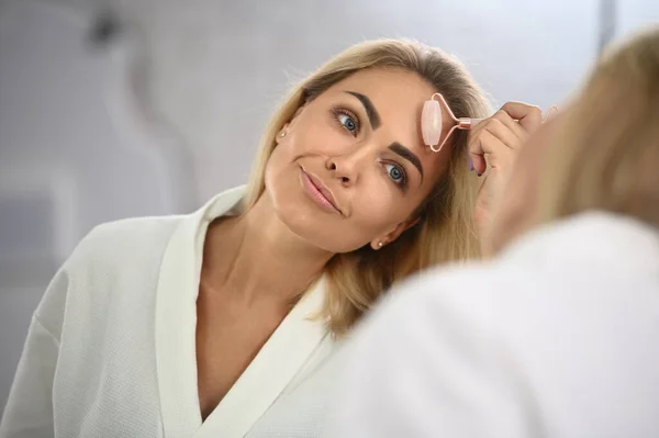 Smiling Young Woman Looking Her Mirror Reflection Massaging Her Face — Stok fotoğraf