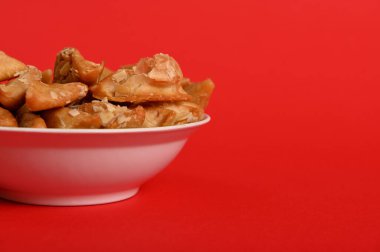 Isolated studio shot on red background of cropped plate with delicious Arabian Moroccan dessert for religious events on a plate. Copy space. Arabic traditional oriental sweets on the festive table