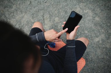 High angle view of a sportsman pointing index finger on a blank screen of a smartphone in his hand. Copy space for mobile application