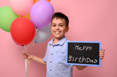 Mutlu ve gülümseyen genç çocuk bir elinde renkli balonlar diğer elinde ise üzerinde 