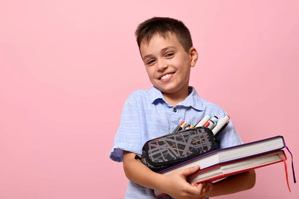 書籍や文房具がいっぱいの鉛筆ケースでピンクの背景にポーズをとる笑顔の学校の少年 学校に戻る テキストの顔の感情と空間を持つ概念 — ストック写真