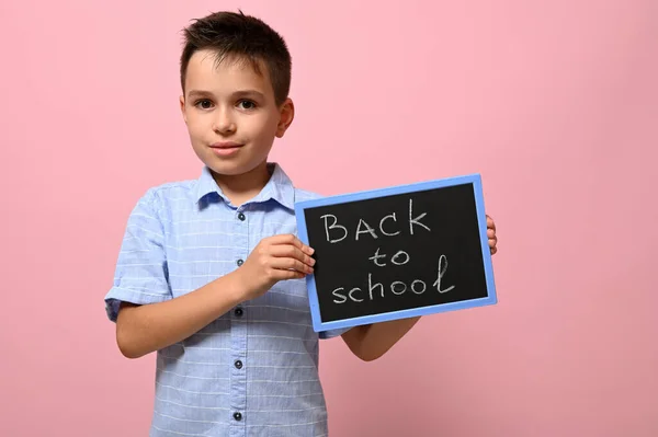 チョークレタリングで黒板を持つ可愛い男の子 学校に戻る テキストのためのスペースとピンクの背景に隔離された — ストック写真