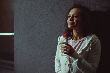 Gri arka planda bir şişe suyu olan güzel, karışık ırk sporcusu.