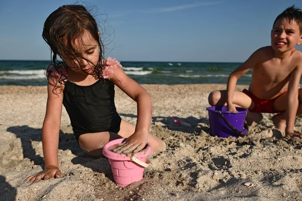 Χαριτωμένο Κορίτσι Γεμίζει Ένα Ροζ Πλαστικό Κουβά Παιχνίδι Άμμο Για — Φωτογραφία Αρχείου