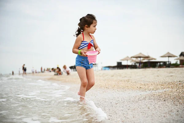 Κοριτσάκι Πολύχρωμο Μαγιό Που Περπατάει Στην Παραλία Ένα Ροζ Κουβά — Φωτογραφία Αρχείου