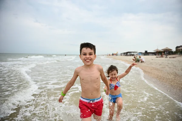Szczęśliwy Przystojny Chłopiec Czerwonych Kąpielówkach Prowadzący Swoją Młodszą Siostrę Rękę — Zdjęcie stockowe