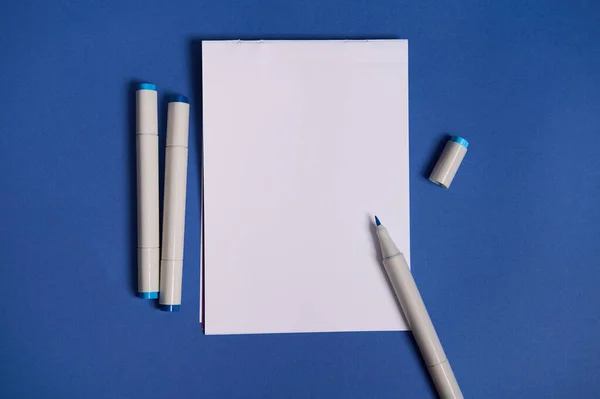 水彩マーカー付きの2色のフラットレイ構成または青の背景に隔離されたコピースペースと紙の白い空白のシートを持つフェルト先端ペン — ストック写真
