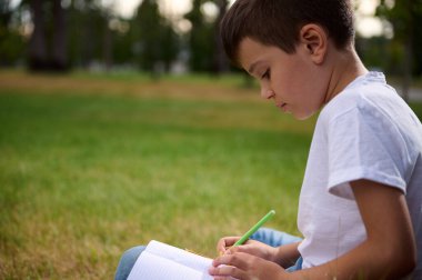 Sevimli, yaşlı, zeki bir öğrencinin portresi, ödev yapan zeki bir okul çocuğu, matematik ödevlerini çözen, açık havada çalışmaktan keyif alan. Okula, bilgiye, eğitime, bilgelik kavramlarına