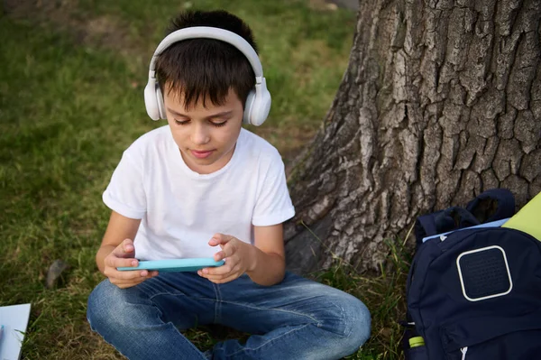 Uroczy Przystojny Uczeń Wieku Podstawówki Noszący Słuchawki Bezprzewodowe Skupiony Zabawie — Zdjęcie stockowe