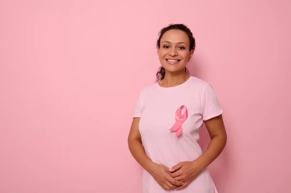 Uluslararası Göğüs Kanseri Gününü sembolize eden pembe saten kurdeleli pembe tişörtlü, gülümseyen bir ırk kadını göğüs kanseri hastaları ve hayatta kalanlara destek ve dayanışma gösteriyor. 1 Ekim