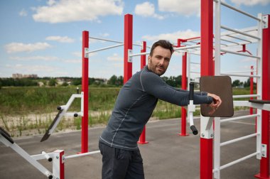 Çekici ve yakışıklı Avrupalı kaslı erkek sporcunun yan portresi. Çapraz bariyerlerin arkasında antrenman yaptıktan sonra başka tarafa bakıyor.