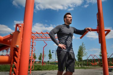 Yakışıklı Avrupalı sporcu bir sporcunun belinde koluyla spor sahasında dikilip başka tarafa bakan kendinden emin portresi. Spor kıyafetli yakışıklı beyaz adam antrenmandan sonra dinleniyor.