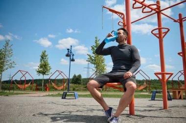 Orta yaşlı sporcu, Kafkas sporcusu güzel, güneşli bir günde dışarıda antrenman yaptıktan sonra şişeden su içer. Yakışıklı Avrupalı adam spor yaptıktan sonra vücudunu sulandırıyor.