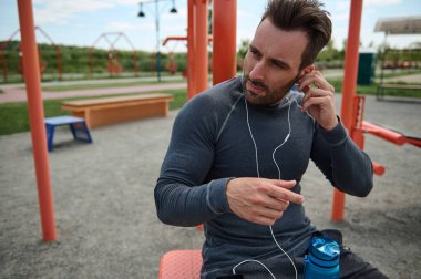 Çekici, maço, Avrupalı, kulaklık takan ve yaz sporları sahasında spor makinesinde oturan beyaz tenli bir sporcunun vesikalığı. Yakın plan portre