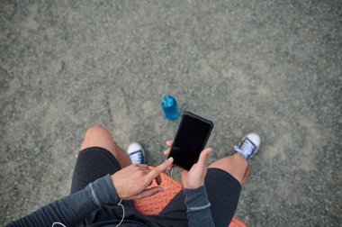 Akıllı telefon tutan bir sporcunun üst görüntüsü ve fotokopi alanı olan siyah boş bir ekrana parmağını doğrultuyor. Atletizm, mobil uygulamadan kalp atışlarını kontrol ediyor